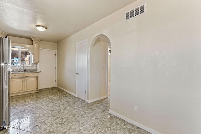 empty room with a sink, visible vents, baseboards, and arched walkways