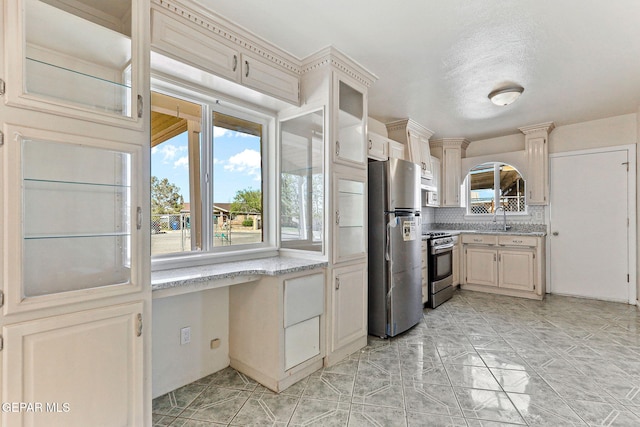 kitchen featuring light stone counters, tasteful backsplash, glass insert cabinets, a sink, and stainless steel appliances