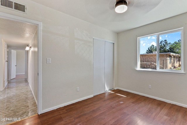 empty room with wood finished floors, visible vents, and baseboards