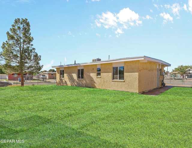 rear view of house with a lawn, stucco siding, and fence