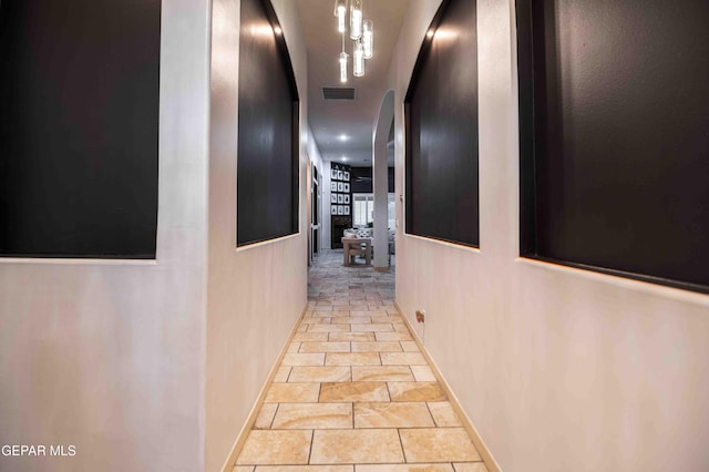 hallway with arched walkways, stone finish floor, visible vents, and baseboards