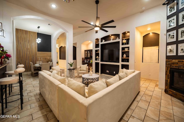 living area with built in shelves, ceiling fan, arched walkways, a fireplace, and recessed lighting