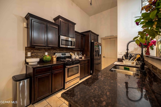 kitchen featuring dark stone counters, dark brown cabinets, a sink, decorative backsplash, and stainless steel appliances
