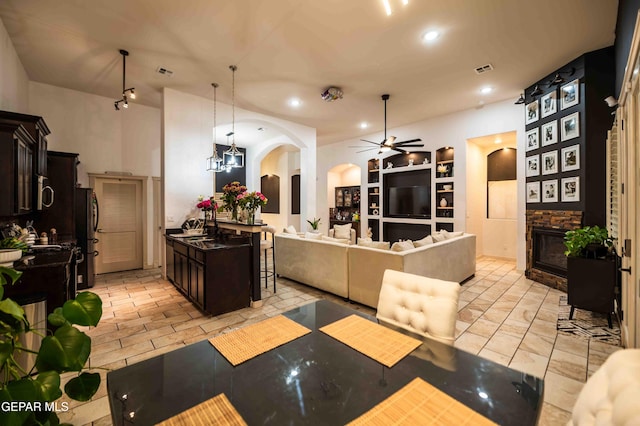 kitchen with arched walkways, open floor plan, ceiling fan, a breakfast bar, and a stone fireplace