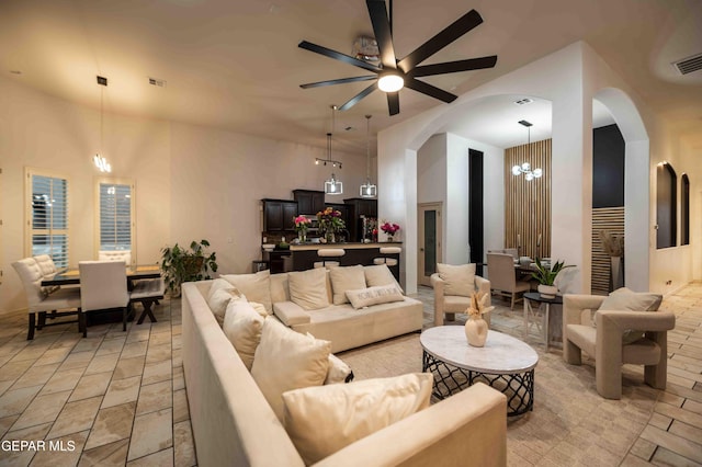 living room with arched walkways, a towering ceiling, visible vents, and ceiling fan with notable chandelier