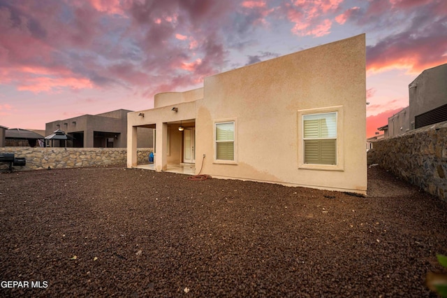 back of house at dusk featuring stucco siding and fence