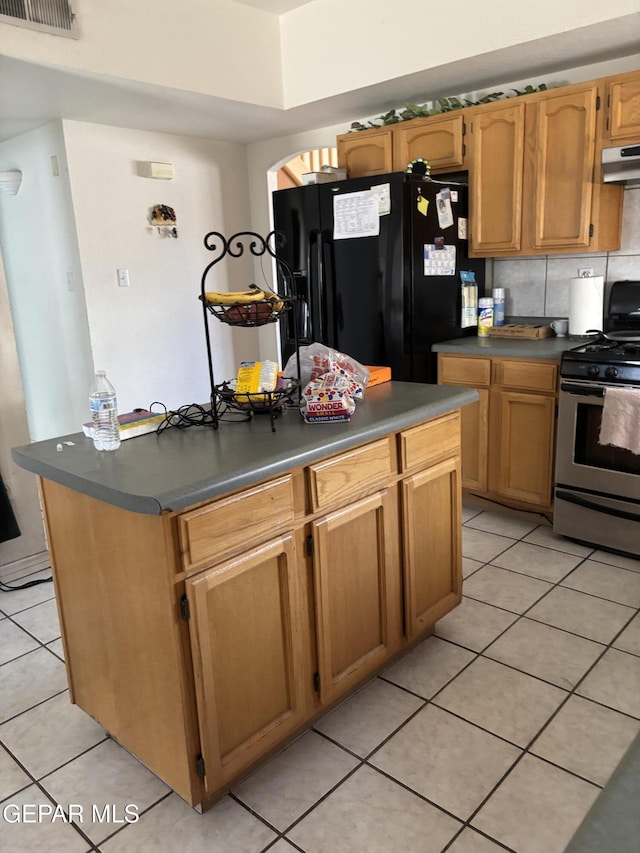 kitchen featuring black fridge with ice dispenser, stainless steel range with gas cooktop, light tile patterned floors, visible vents, and dark countertops
