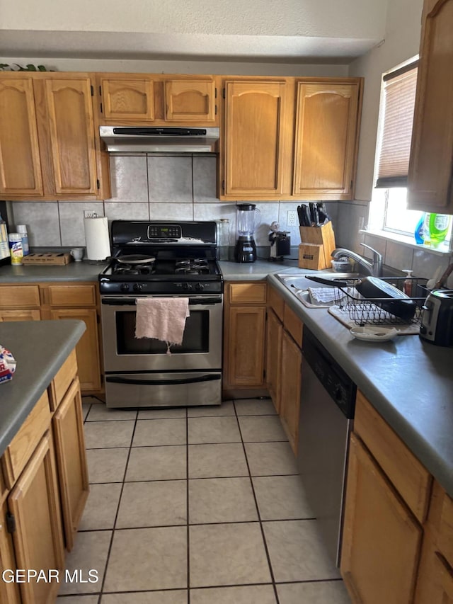 kitchen featuring stainless steel appliances, light tile patterned flooring, under cabinet range hood, and decorative backsplash