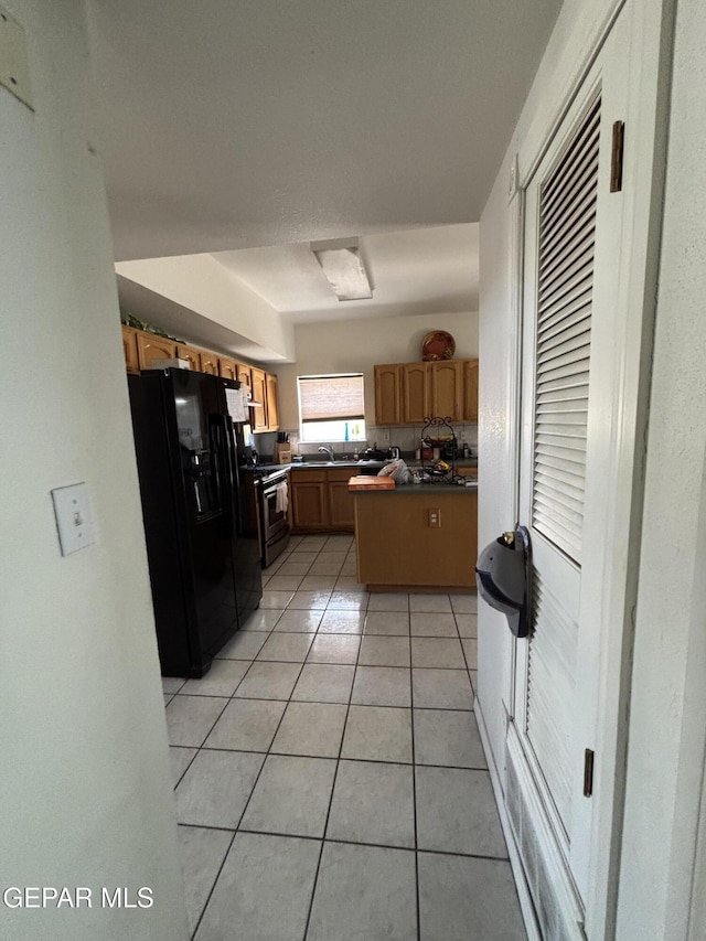 kitchen with light tile patterned floors, a sink, dark countertops, gas range, and black fridge