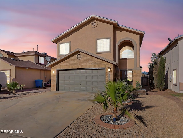 traditional-style home featuring concrete driveway, an attached garage, stucco siding, and brick siding