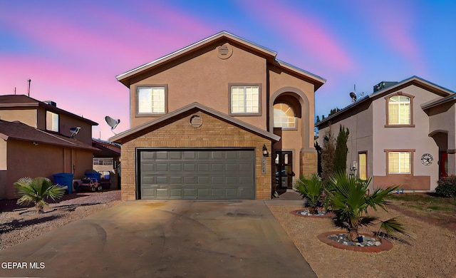 view of front of home featuring an attached garage, concrete driveway, stucco siding, and brick siding