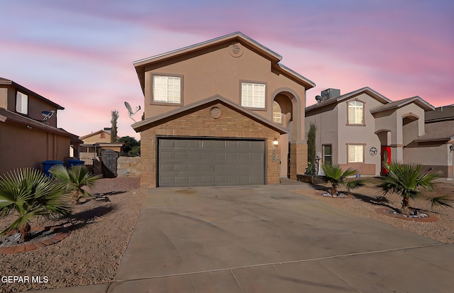 view of front of home featuring driveway, stucco siding, brick siding, and a garage