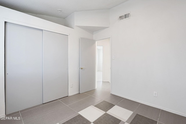 unfurnished bedroom with lofted ceiling, baseboards, a closet, and visible vents