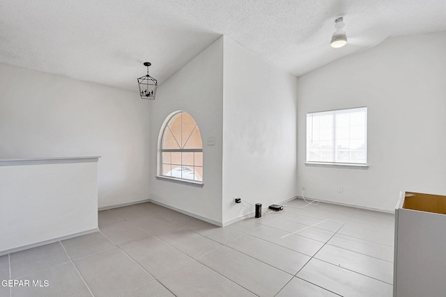 spare room featuring light tile patterned floors, lofted ceiling, and a textured ceiling
