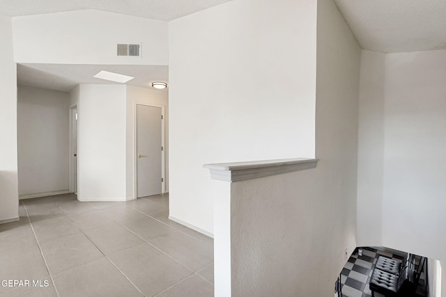 hallway with baseboards, a textured ceiling, visible vents, and light tile patterned flooring