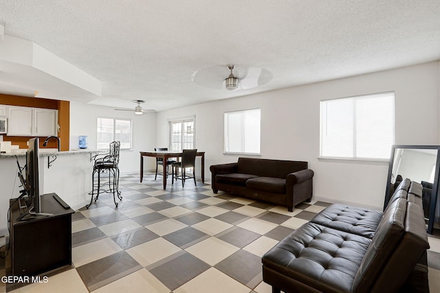 living area featuring light floors, ceiling fan, and a textured ceiling