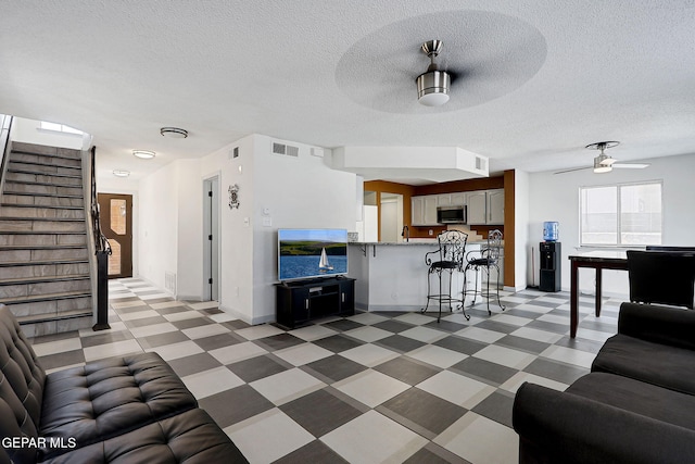 living room with light floors, visible vents, stairway, a ceiling fan, and baseboards