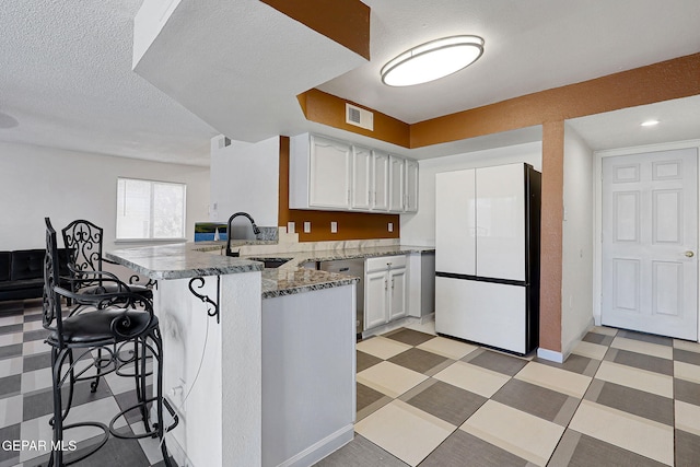 kitchen with freestanding refrigerator, a peninsula, visible vents, and white cabinets