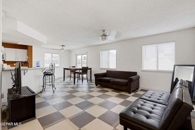 living area with light floors, a textured ceiling, baseboards, and a ceiling fan