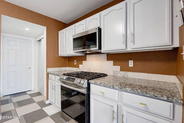 kitchen with white cabinetry, light floors, stainless steel appliances, and light stone countertops