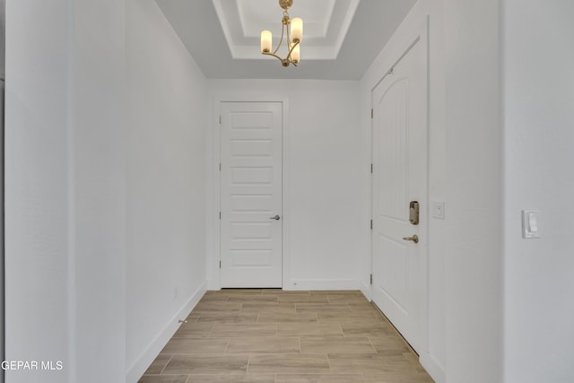 doorway featuring baseboards, light wood-style floors, and a raised ceiling