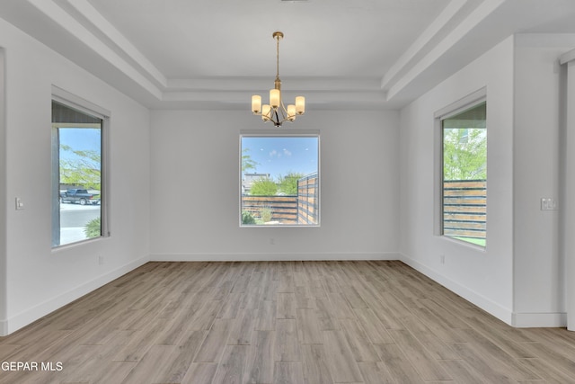 empty room with light wood-type flooring, baseboards, a tray ceiling, and a chandelier