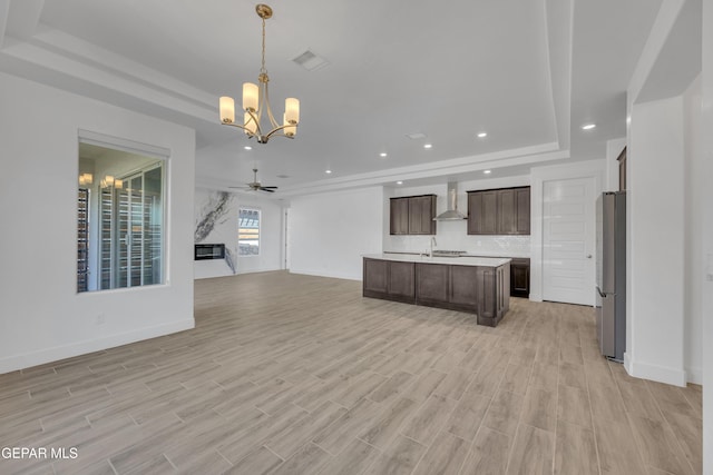 kitchen with a tray ceiling, dark brown cabinets, light countertops, freestanding refrigerator, and open floor plan