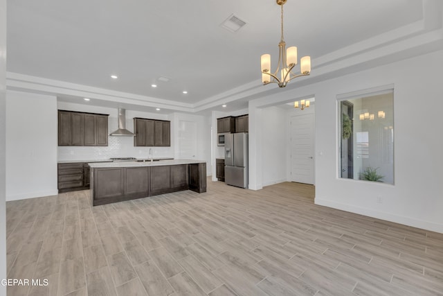 kitchen with wall chimney exhaust hood, a tray ceiling, stainless steel fridge, an inviting chandelier, and light countertops