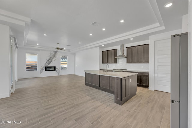 kitchen with a raised ceiling, wall chimney exhaust hood, freestanding refrigerator, and a sink