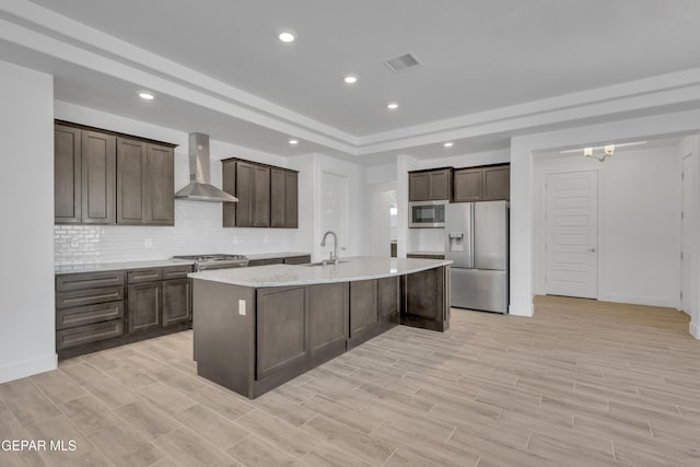 kitchen with stainless steel appliances, backsplash, a raised ceiling, a sink, and wall chimney exhaust hood