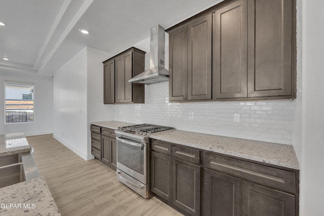 kitchen featuring tasteful backsplash, wall chimney exhaust hood, baseboards, and stainless steel gas stove