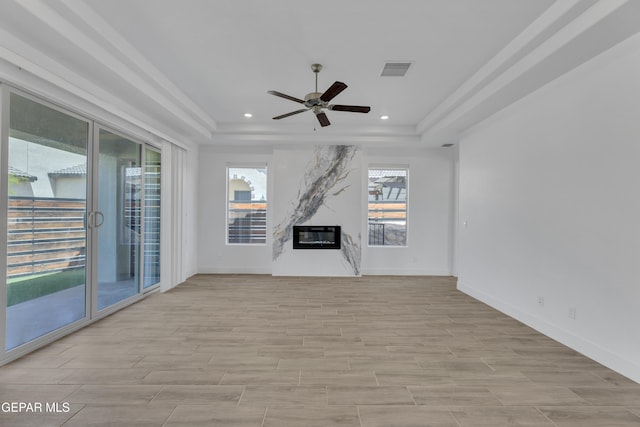 unfurnished living room featuring a raised ceiling, visible vents, a ceiling fan, and light wood finished floors