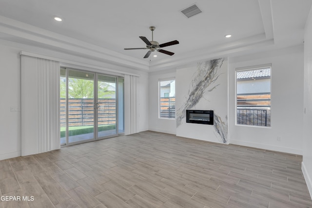 unfurnished living room featuring light wood finished floors, a tray ceiling, visible vents, a ceiling fan, and a fireplace