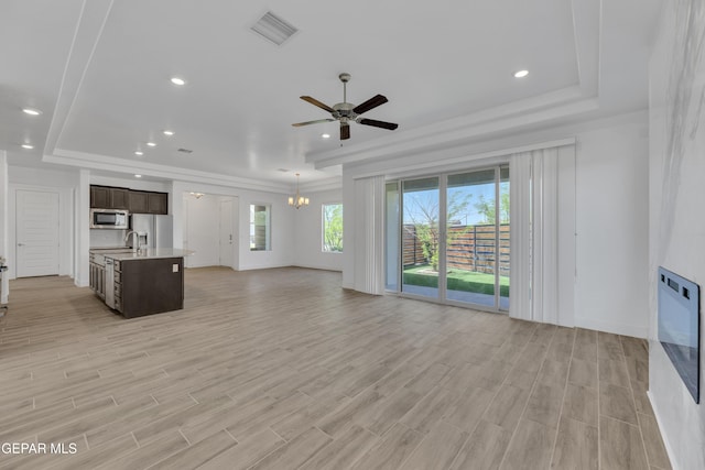 unfurnished living room featuring a sink, ceiling fan with notable chandelier, light wood finished floors, a raised ceiling, and visible vents