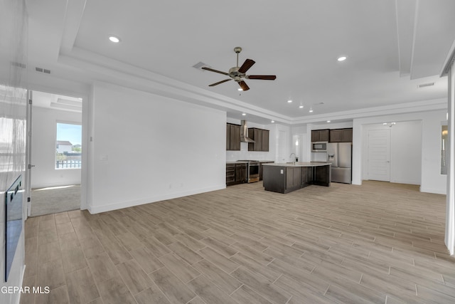 kitchen with wall chimney exhaust hood, stainless steel appliances, open floor plan, dark brown cabinetry, and a raised ceiling