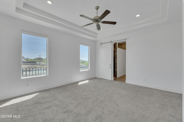 unfurnished bedroom featuring a barn door, a raised ceiling, carpet, and baseboards
