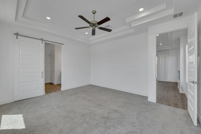 unfurnished bedroom with a tray ceiling, carpet floors, visible vents, and a barn door
