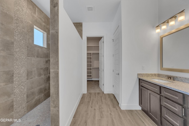 bathroom with baseboards, walk in shower, vanity, and visible vents