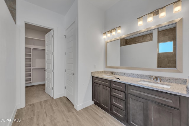 full bathroom featuring double vanity, a spacious closet, baseboards, and a sink
