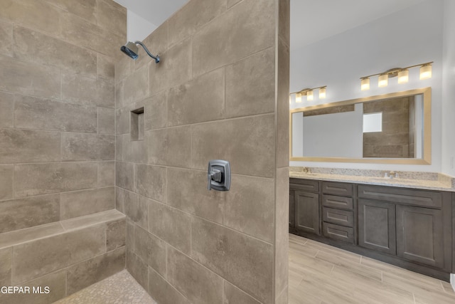 bathroom featuring wood finished floors, a sink, double vanity, and tiled shower