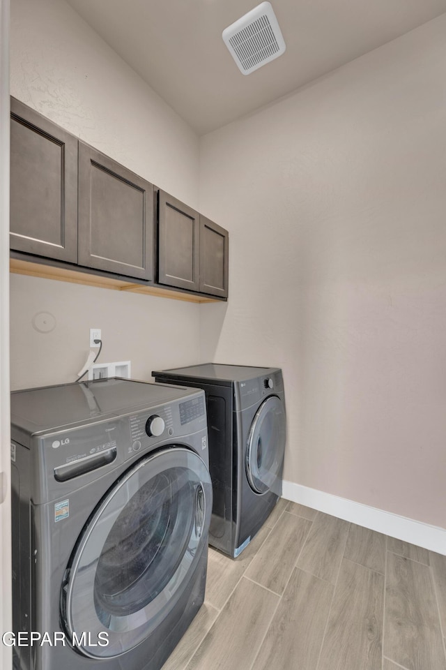 clothes washing area featuring baseboards, visible vents, independent washer and dryer, cabinet space, and wood finish floors