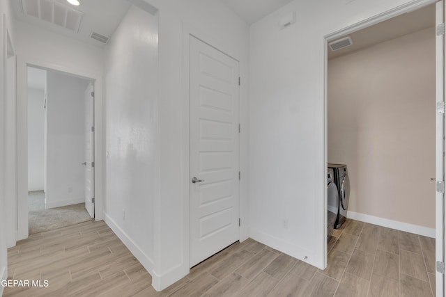 hall featuring wood tiled floor, independent washer and dryer, visible vents, and baseboards