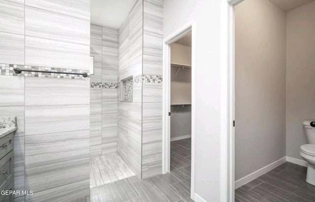 full bathroom featuring baseboards, toilet, wood finish floors, vanity, and a walk in closet