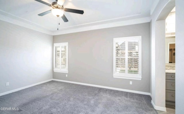 carpeted empty room with ceiling fan, baseboards, a tray ceiling, and arched walkways