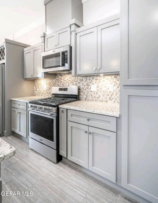 kitchen with light stone counters, gray cabinetry, stainless steel appliances, and tasteful backsplash