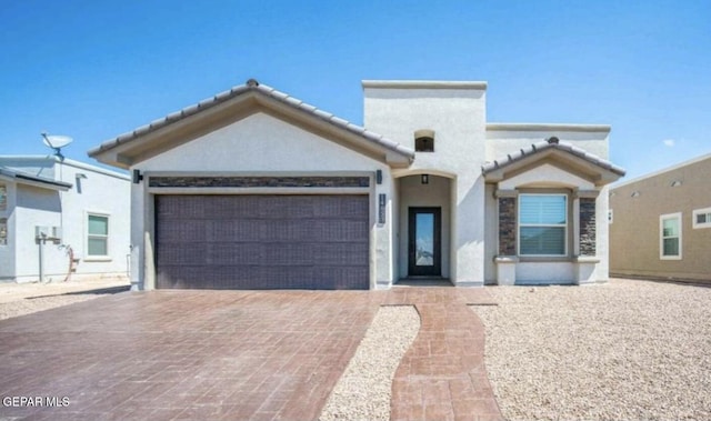 view of front facade featuring a garage, stucco siding, a tile roof, and decorative driveway