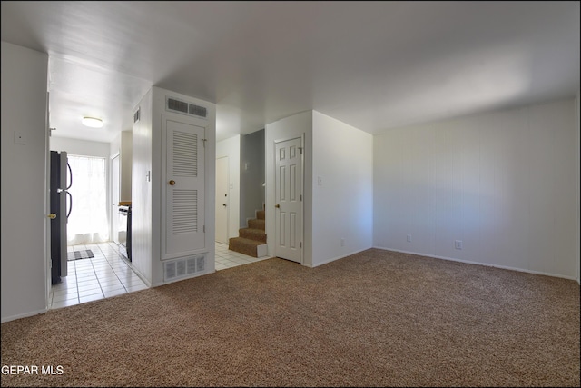 unfurnished room featuring visible vents, light tile patterned floors, light carpet, and stairway