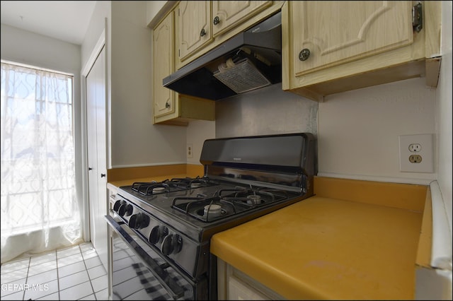 kitchen featuring cream cabinets, light tile patterned floors, under cabinet range hood, light countertops, and range with gas cooktop