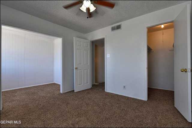 unfurnished bedroom with carpet, a closet, a walk in closet, visible vents, and a textured ceiling