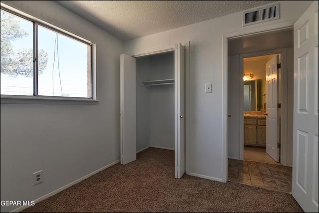 unfurnished bedroom featuring a textured ceiling, visible vents, baseboards, a closet, and light carpet